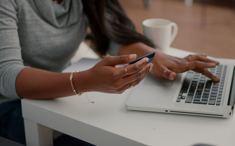 Femme d'affaires qui annote des documents à la main devant son ordinateur portable, près d'une fenêtre lumineuse